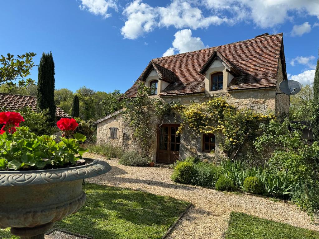 une vieille maison en pierre avec des fleurs rouges dans une cour dans l'établissement Petit Loulet, à Puylagarde