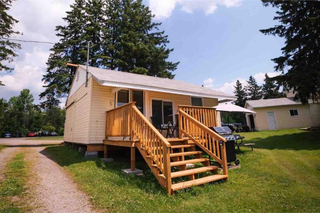 een klein huis met een groot houten terras bij Beachfront Cabin #5- Maijac Resort & Marina in Magnetawan