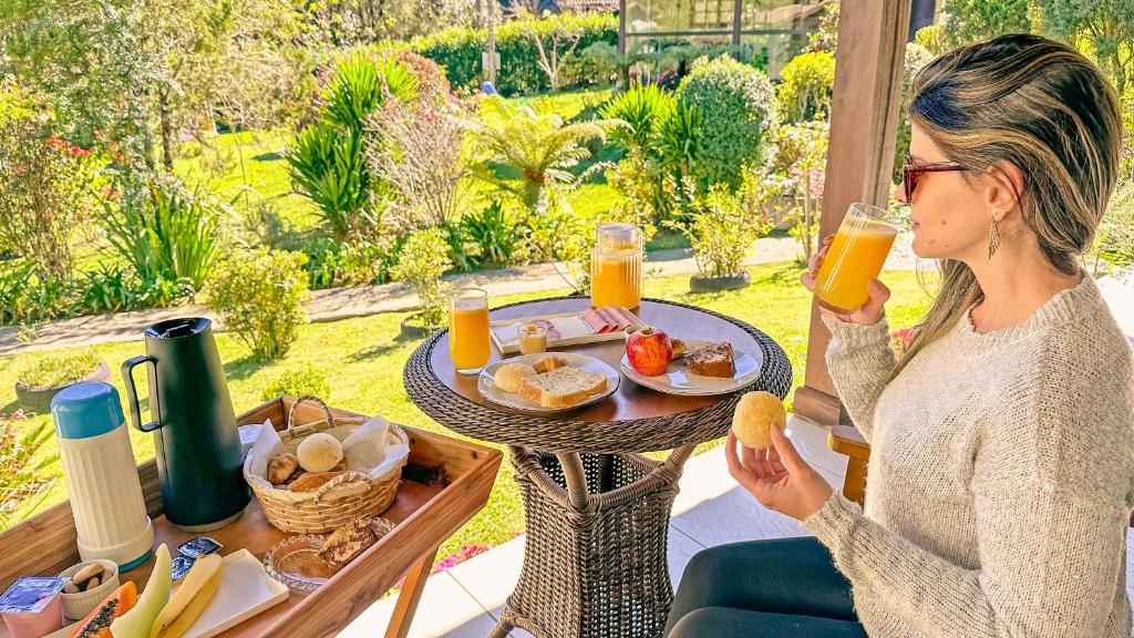 a woman drinking a glass of orange juice at Pousada Medeiros in Monte Verde