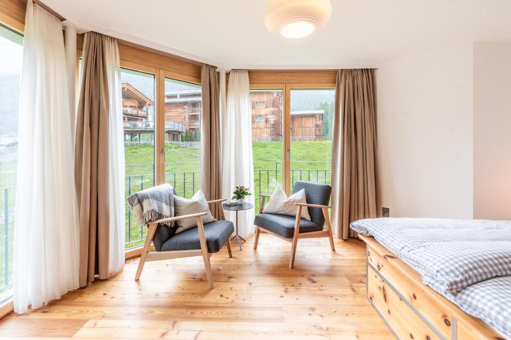 a bedroom with a bed and two chairs and windows at Studio Haro in Zermatt