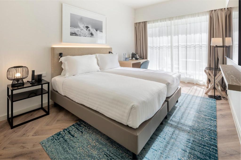 a bedroom with a large white bed with a blue rug at Crowne Plaza - Caparica Lisbon in Costa da Caparica