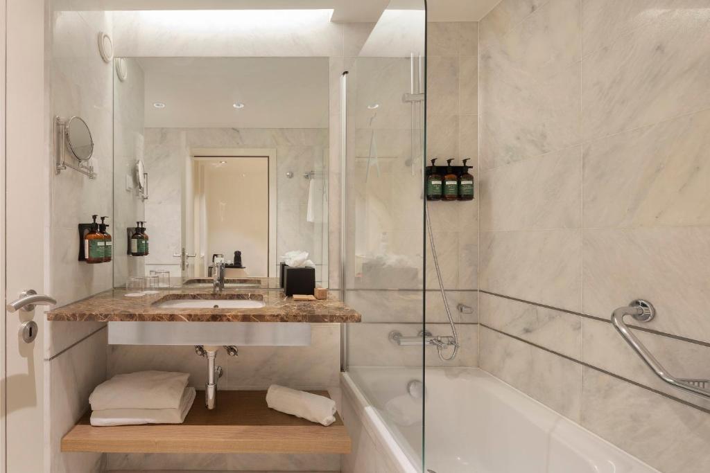 a bathroom with a sink and a tub and a mirror at Crowne Plaza - Caparica Lisbon in Costa da Caparica