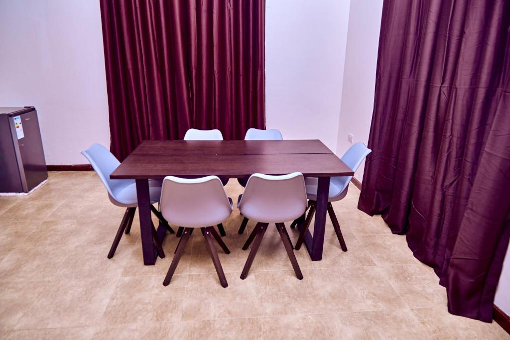 Una mesa y sillas de madera en una habitación con cortinas rojas. en Mount Meru View Homestay, en Arusha