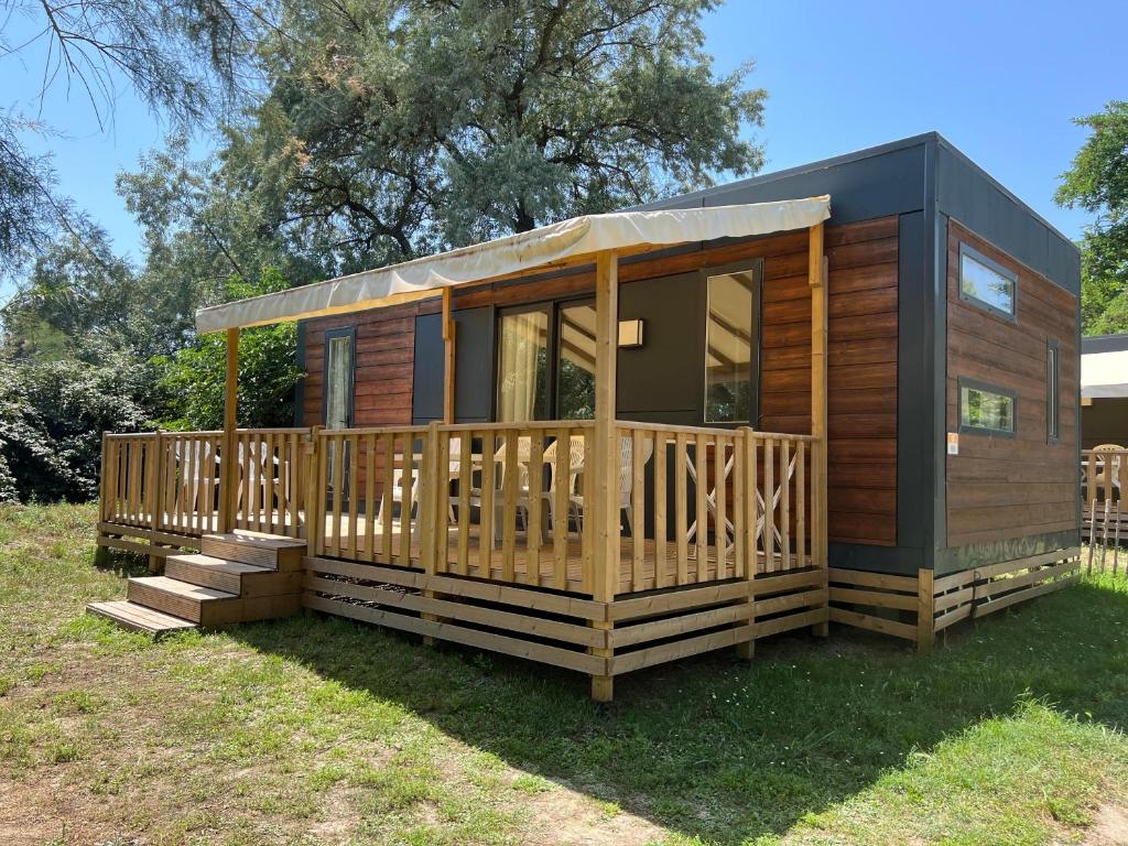 une cabane en bois avec une grande terrasse sur l'herbe dans l'établissement MobilHome Comfort XL (37m2) : 2 Chambres (6 personnes) - 2 SDB - Clim centralisée - TV - Terrasse balcon, à Cadenet