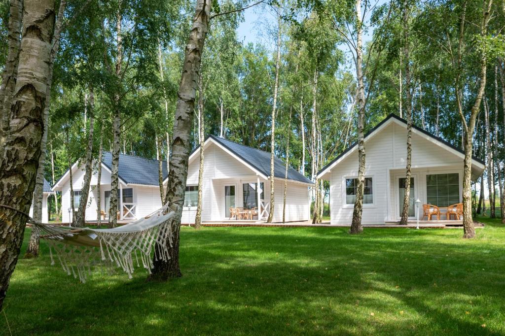two white houses in a yard with trees at Off White Domki Darłówko in Darlowko