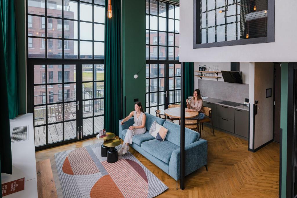 two women sitting on a couch in a room with windows at Hotel de Timmerfabriek I Kloeg Collection in Vlissingen