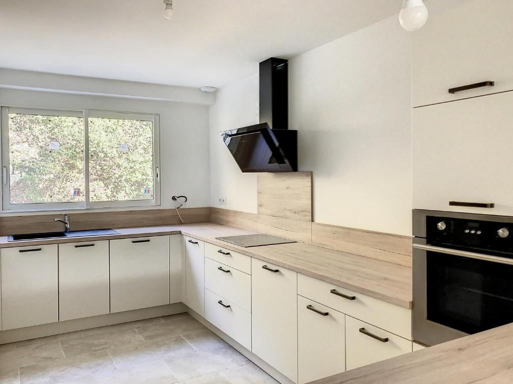 une cuisine avec des armoires blanches, un évier et une fenêtre dans l'établissement Bastide du Safrus, à Villeneuve-lès-Avignon