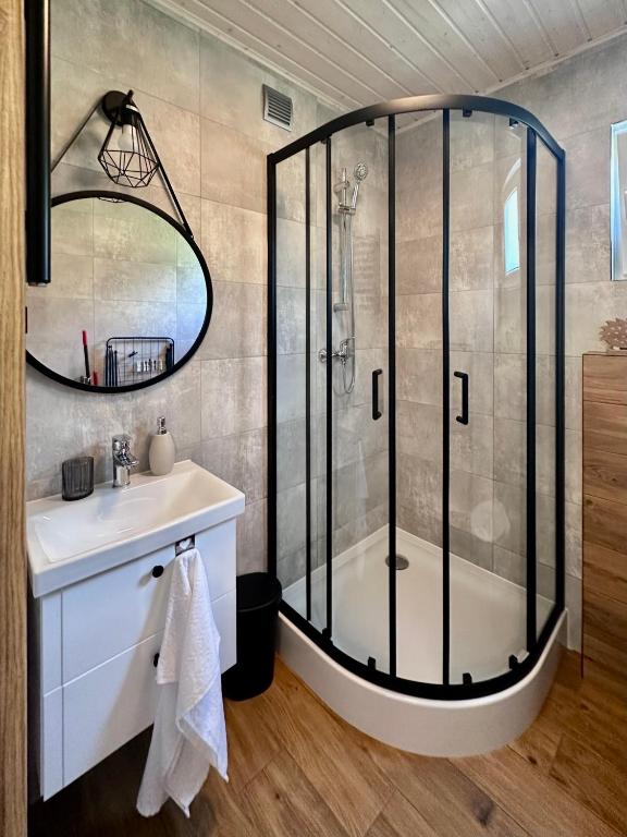 Modern bathroom with glass shower enclosure, round mirror, and wooden accents.