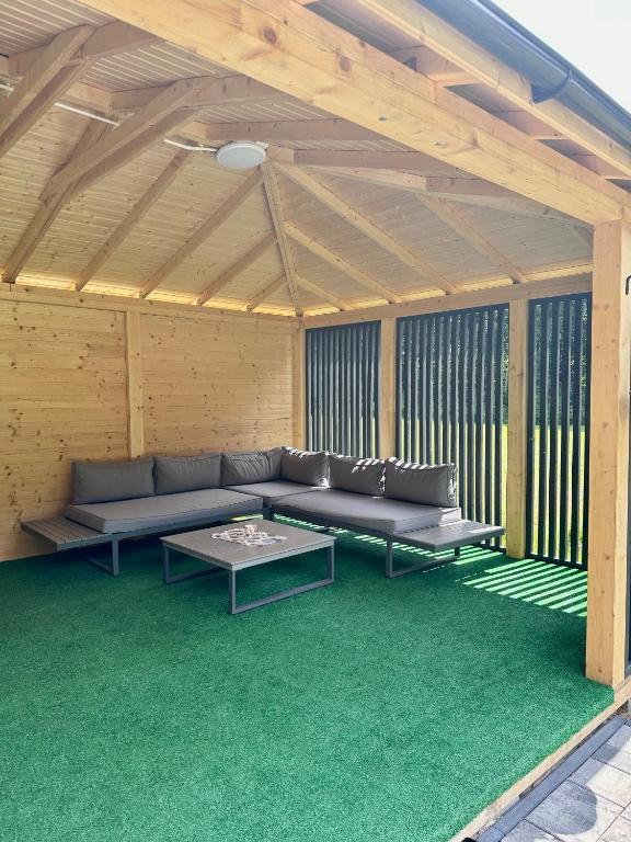 Covered outdoor seating area with gray couches and green carpet.