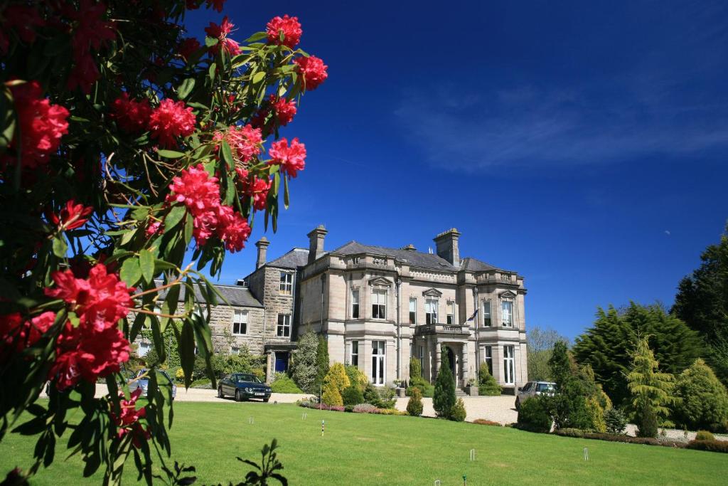 ein altes Herrenhaus mit roten Blumen davor in der Unterkunft Tre-Ysgawen Hall & Spa in Llangefni