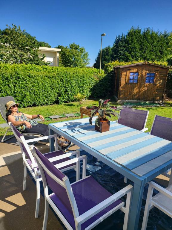 une femme assise à une table bleue dans une cour dans l'établissement Rue des hautes lumières ouistreham Mer et campagne 3 chambres, à Saint-Aubin-dʼArquenay