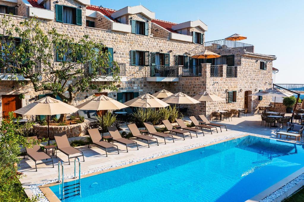 a pool with chairs and umbrellas next to a building at Boutique hotel Ruzmarin SPA & Garden by Aycon in Budva