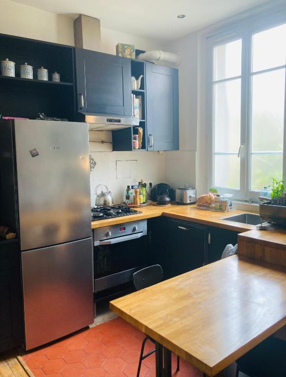 Il comprend une cuisine équipée d'un réfrigérateur en acier inoxydable et d'une table en bois. dans l'établissement Charmant T3 dans les Puces, à Saint-Ouen