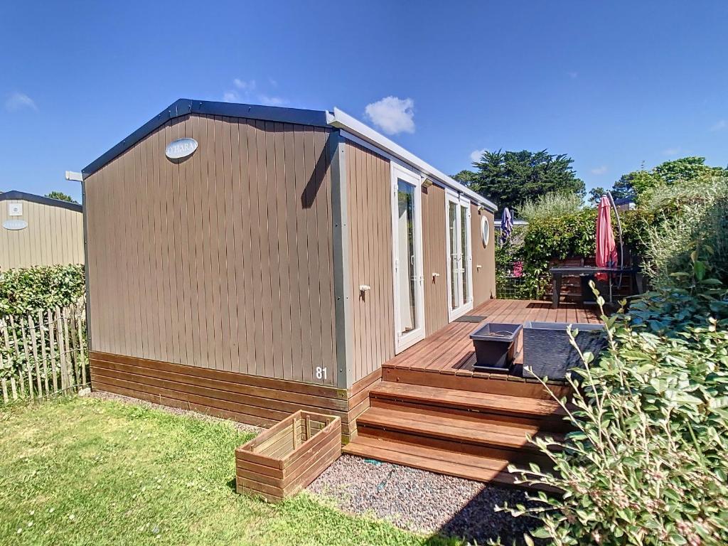 une petite maison avec une terrasse en bois dans une cour dans l'établissement Mobil-home Grand Confort 2 Chambres, Proche Plage, 4 Pers., Piscine Chauffée, Parking, Wi-Fi Gratuit - FR-1-361A-86, à Jullouville