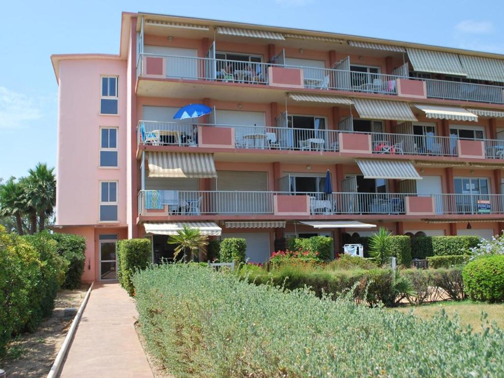 un immeuble d'appartements rose avec balcon et buissons dans l'établissement Studio cabine avec jardin privé face plage du Lavandou - 4 couchages - FR-1-803-52, au Lavandou