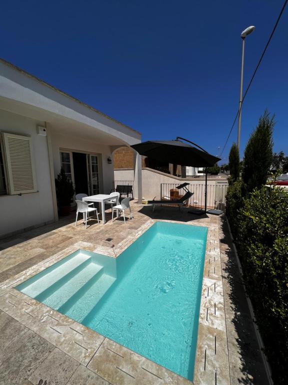 a swimming pool with a table and an umbrella at Villa il Giglio in Marina di Mancaversa