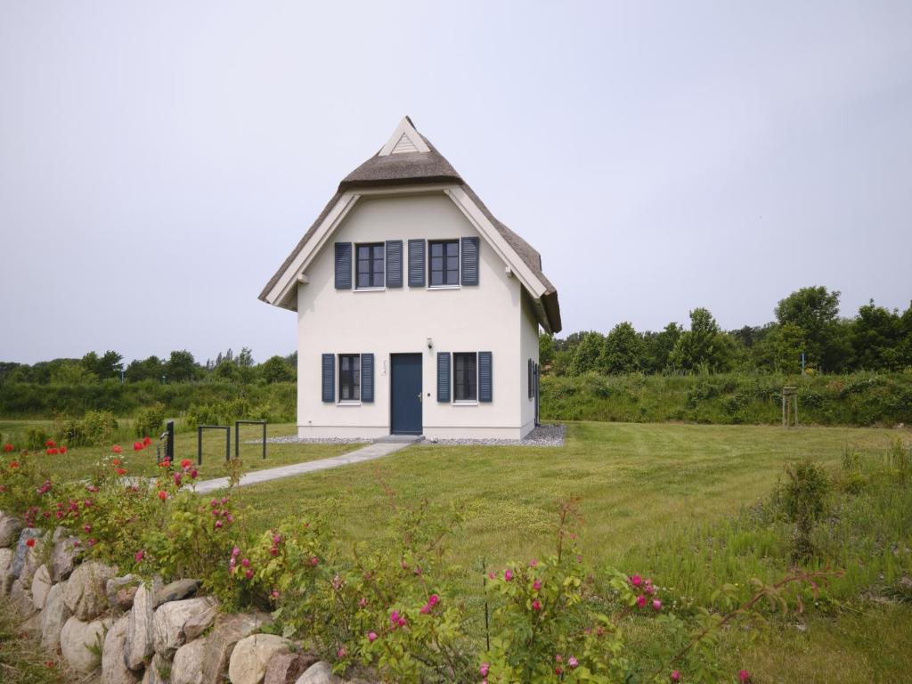 a white house on a field with flowers at Reetland am Meer - Premium Reetdachvilla mit 3 Schlafzimmern, Sauna und Kamin F04 in Dranske