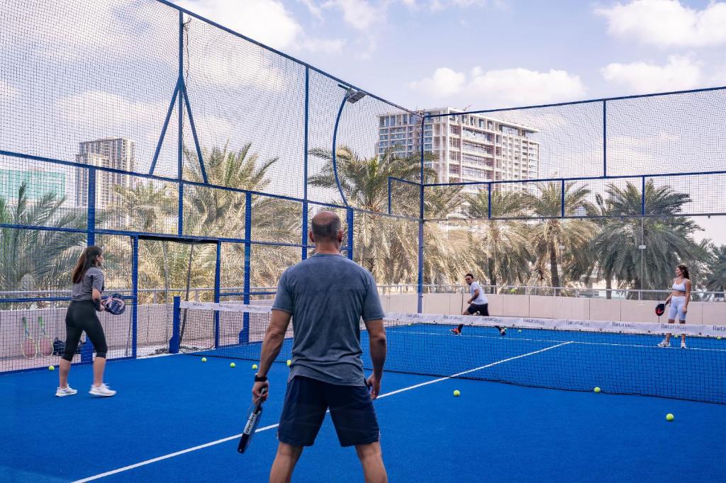 a group of people playing tennis on a tennis court at Beach Rotana - Abu Dhabi in Abu Dhabi