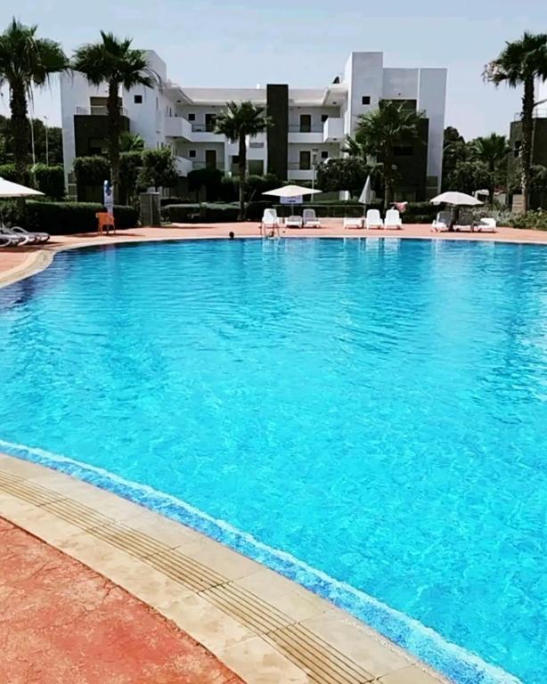 a large blue swimming pool with chairs and umbrellas at Appart Cosy Résidence Perla in Saïdia