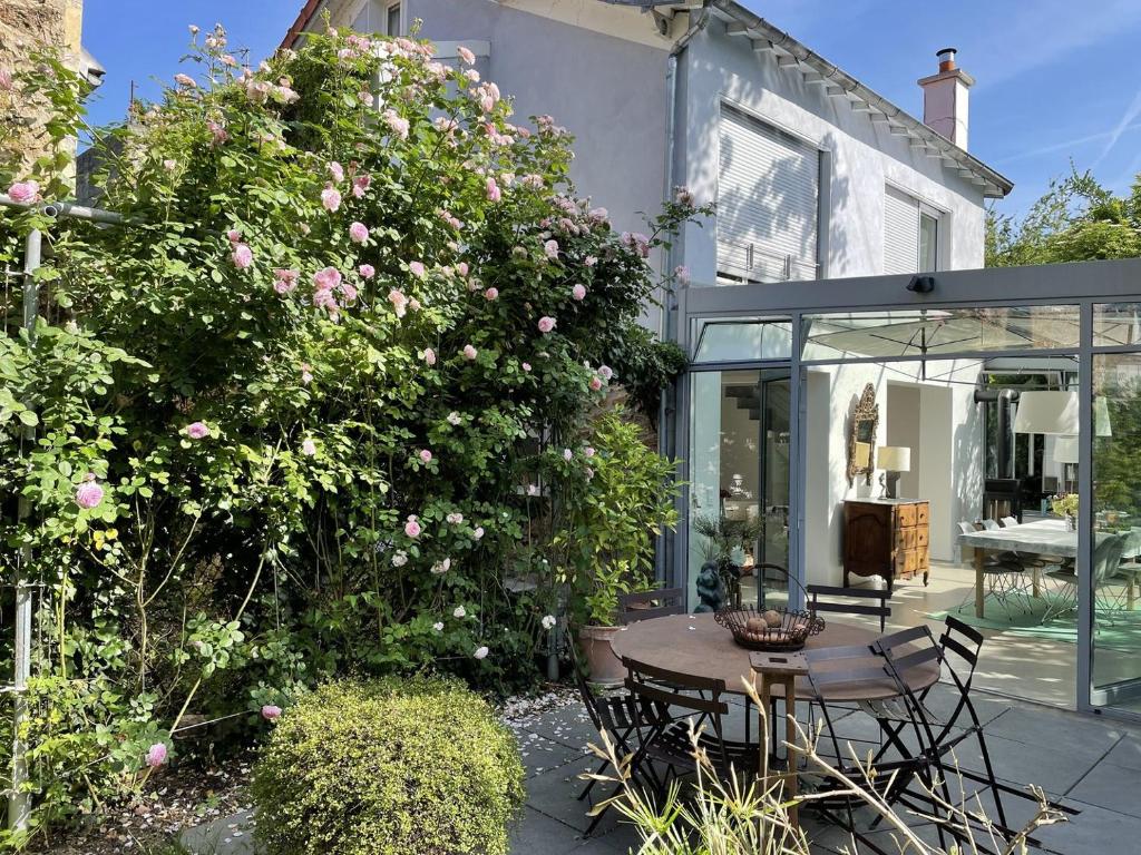 a patio with a table and a bush with pink roses at GuestReady - Charming haven with a private garden in Nogent-sur-Marne