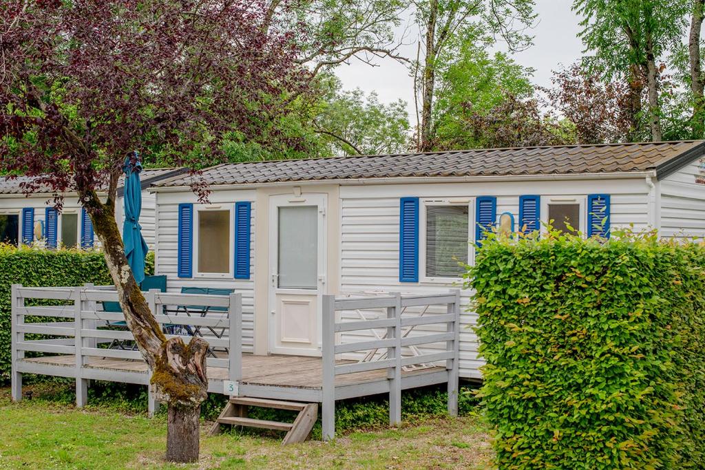 Cette petite maison blanche dispose de fenêtres bleues et d'une terrasse couverte. dans l'établissement Camping Onlycamp La Colombière, à Pesmes