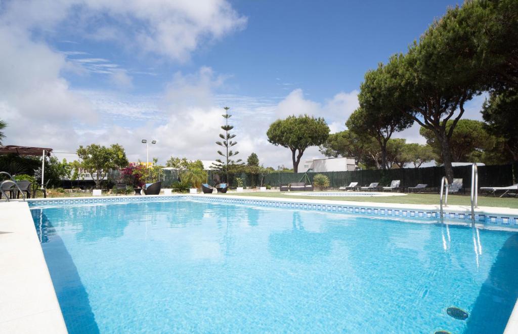 a large blue swimming pool with trees in the background at Hotel Albaida Nature in Mazagón