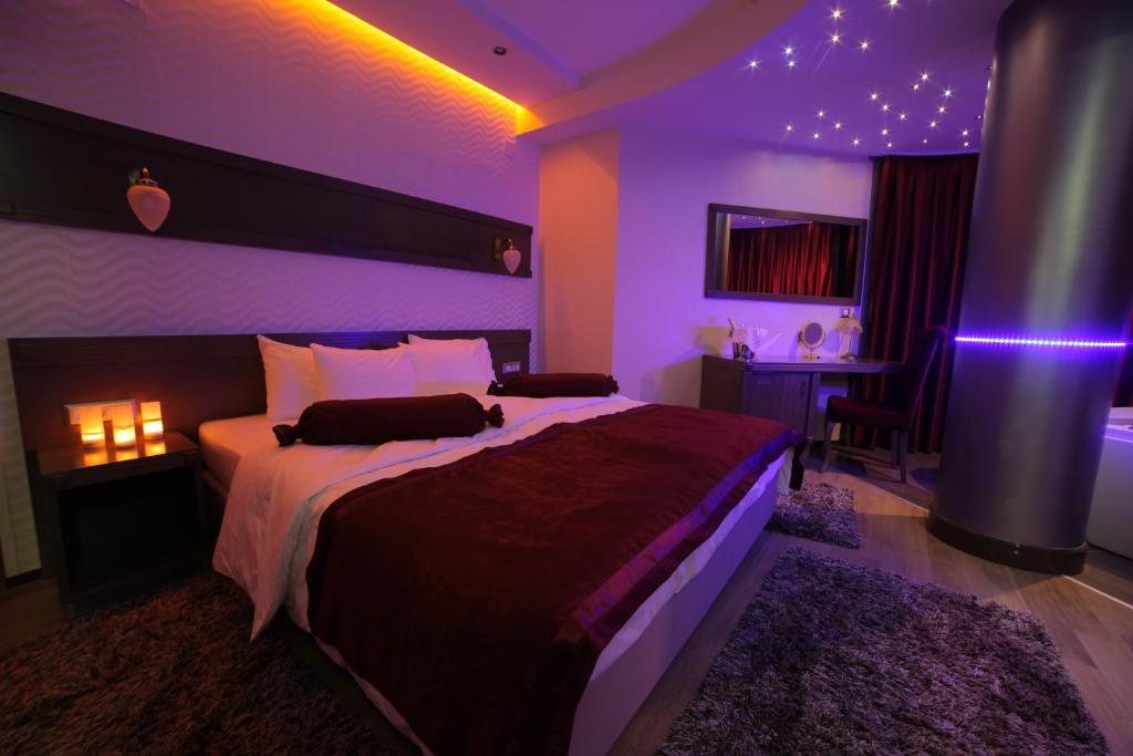 King bed with burgundy linens, bedside lamps and rolled towels, desk with mirror, purple LED ceiling lights and shag rug at City Palace Hotel in Ohrid