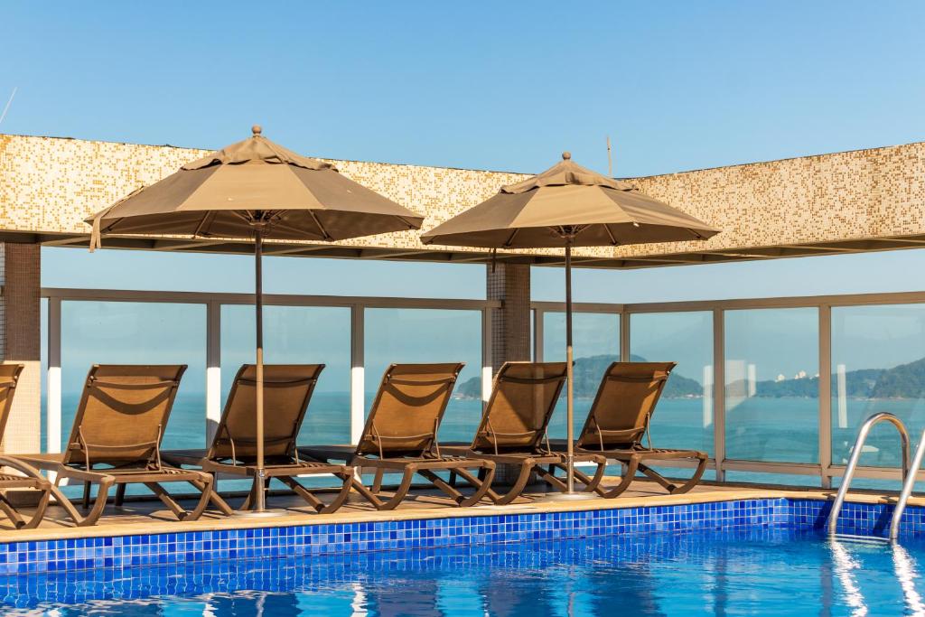 a group of chairs and umbrellas next to a swimming pool at Parque Balneário Hotel Santos by Castelo Itaipava in Santos