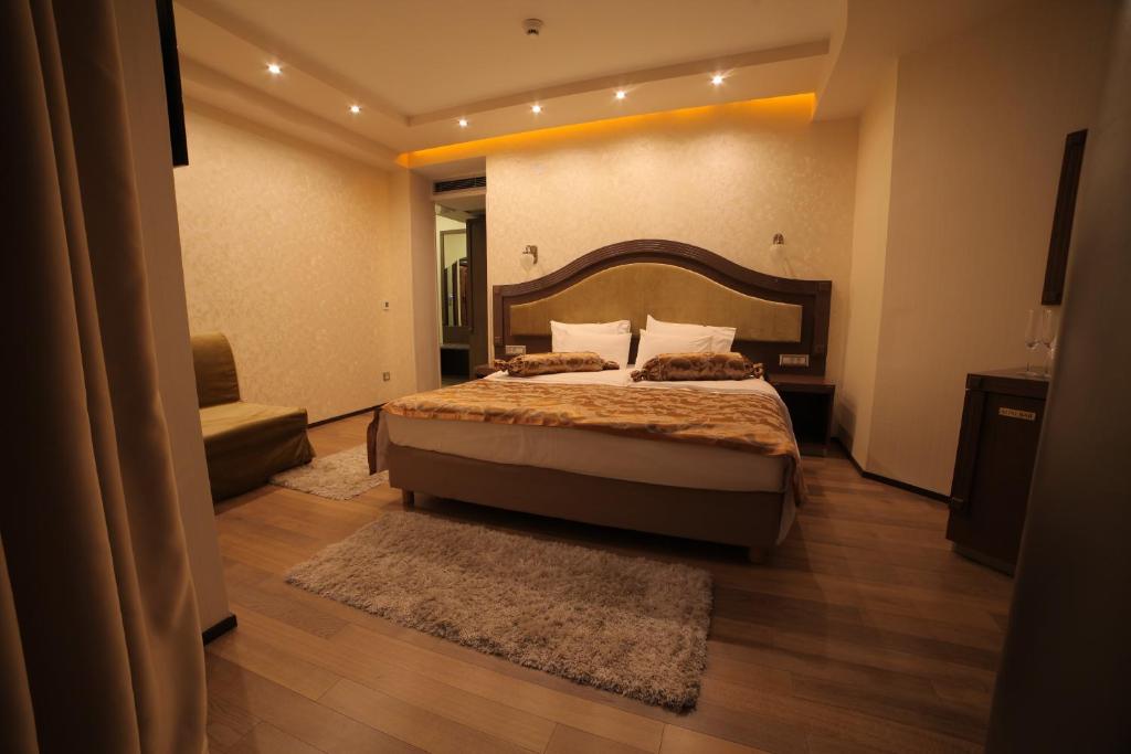 King bed with wooden headboard, bedside tables and lamps, shag rug, seating area and recessed ceiling lighting at City Palace Hotel in Ohrid