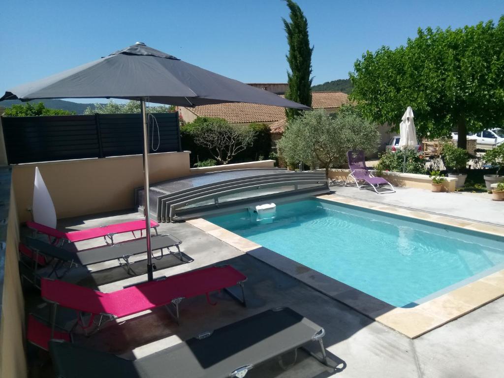 een zwembad met ligstoelen en een parasol bij la bastide aux buis avec piscine in Blauvac