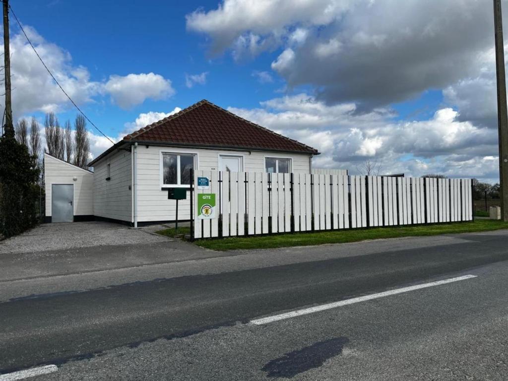 une maison blanche avec une clôture à côté d'une route dans l'établissement Gîte de Charme avec Jardin Privé, Proche de Lille et Hazebrouck, Idéal pour Familles et Cyclistes - FR-1-510-209, à Haverskerque