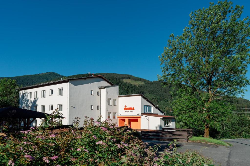a white building with trees and mountains in the background at Retro Hotel JISKRA in Čeladná