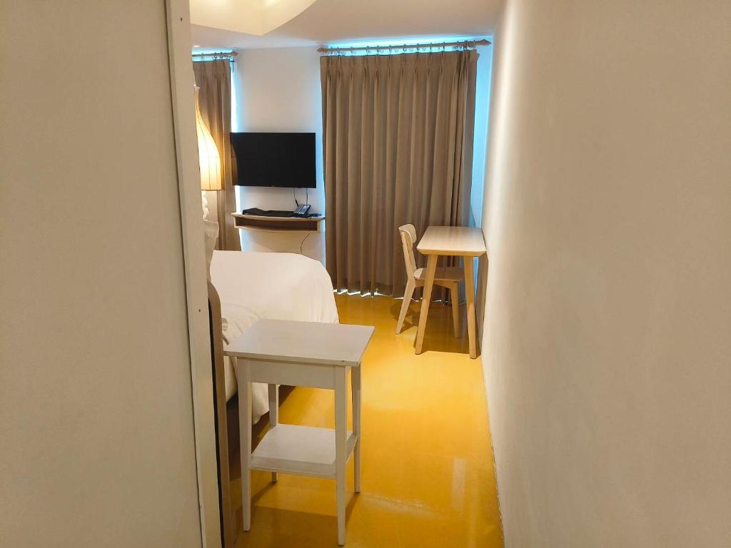 A compact room viewed from the doorway, with a bed, television, small table and drawn curtains.