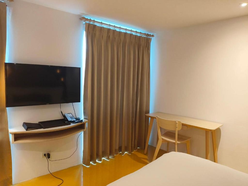 A room corner with a wall-mounted television, curtained window and simple desk.