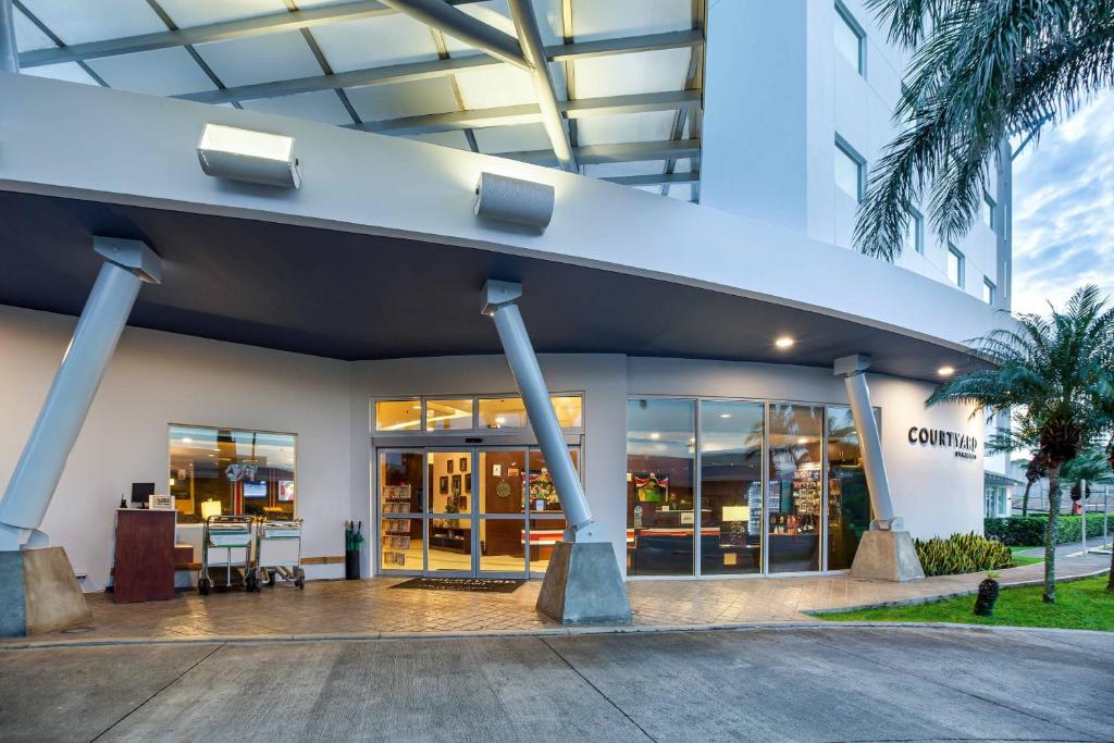 a building with glass doors and palm trees at Courtyard by Marriott San Jose Airport Alajuela in Alajuela City