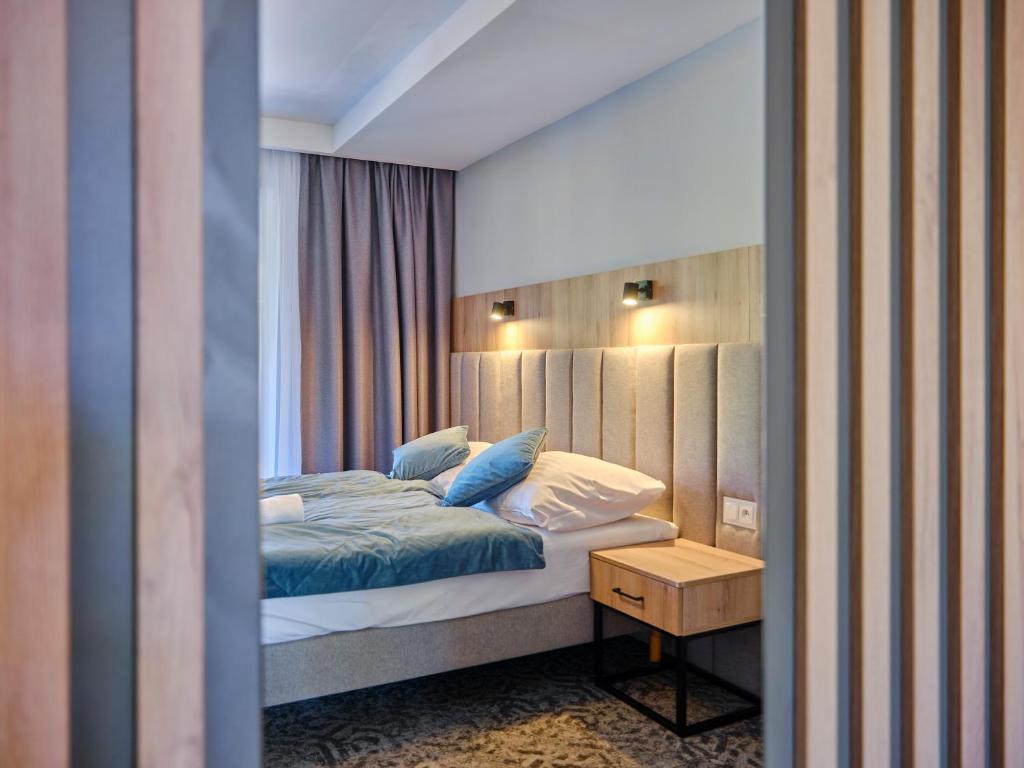 Modern hotel bedroom with upholstered headboard, blue bedding, wall lamps, bedside table, soft ambient lighting.