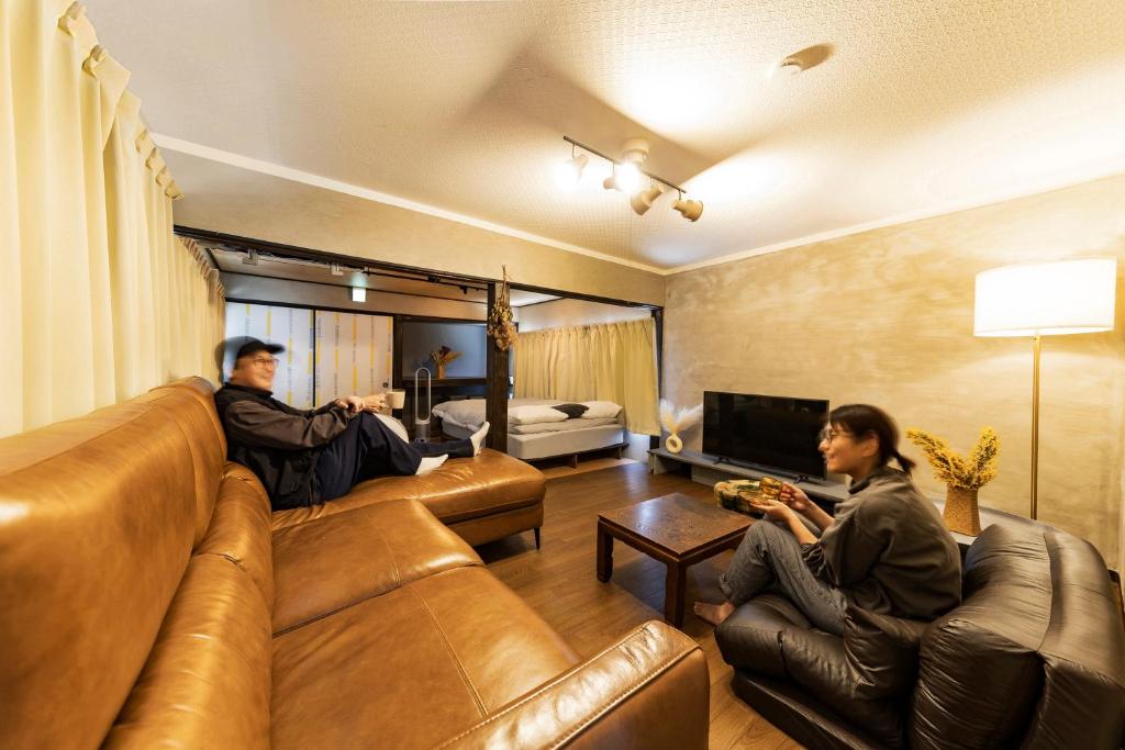 dos personas sentadas en sofás en una sala de estar en Holiday cottage BEPPU ICHIYA, en Beppu