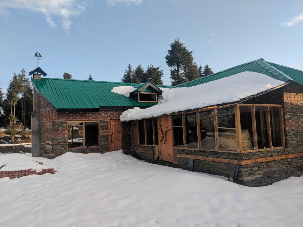 a building with a green roof in the snow at Wild orchid trail cottages in Jhatingr