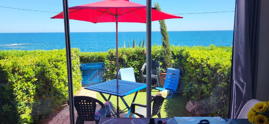 - une table et des chaises avec un parapluie rouge et l'océan dans l'établissement BLEU BOUCHAREL, à Saint-Aygulf
