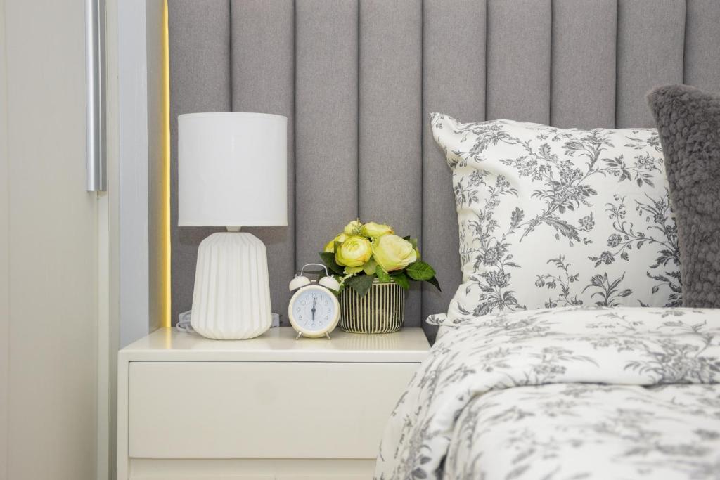 Una cama con una mesita de noche con una lámpara y un reloj. en Le Monaco Suites - Azure North Pampanga, en San Agustin