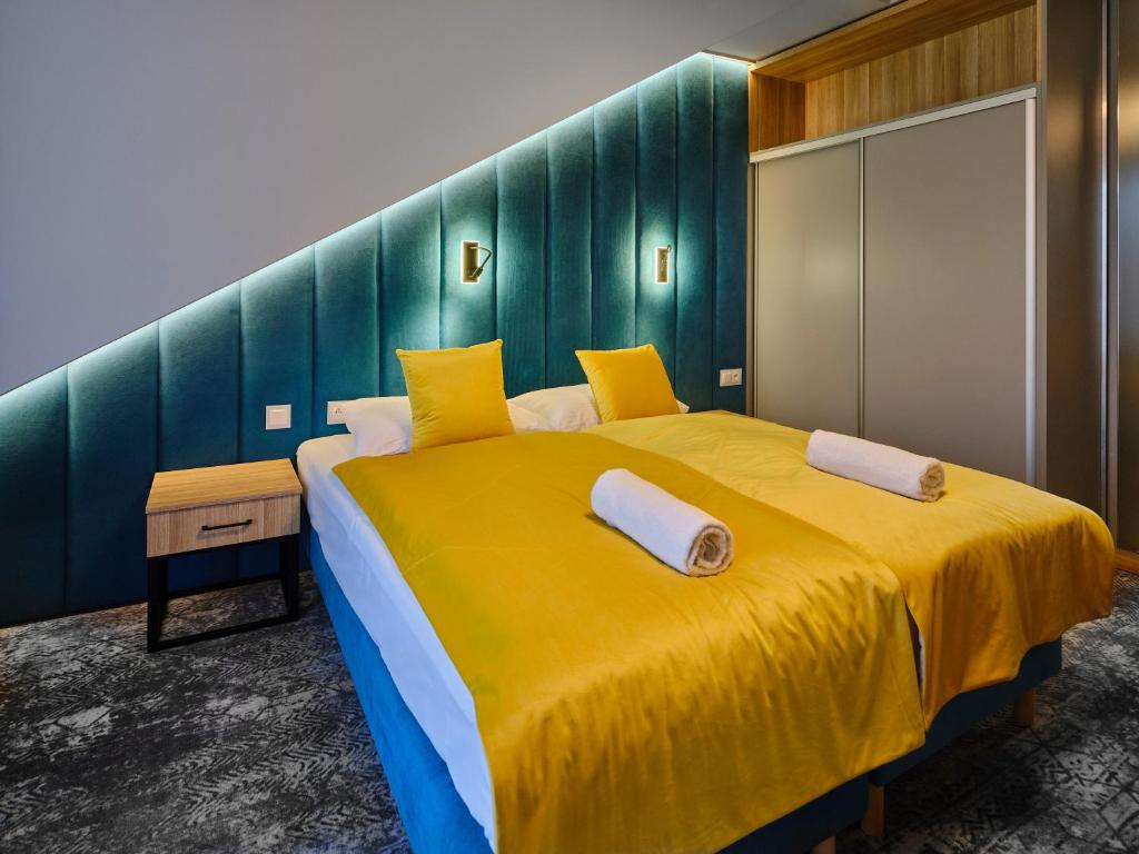 Twin beds with yellow covers against a teal, angled tufted headboard, bedside table included.