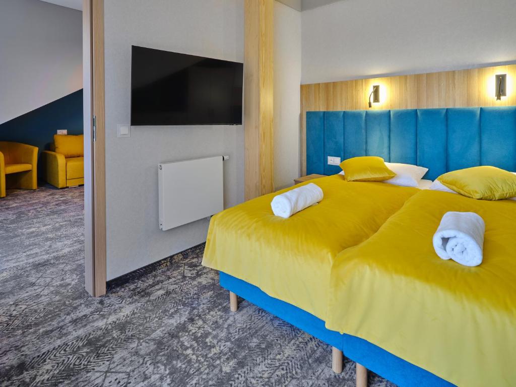 Twin beds with bright yellow duvets and teal headboard, wall TV and seating area visible.