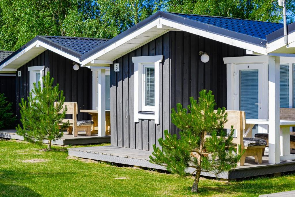 a black cabin with a porch and chairs in a yard at 83 Pylimas Šventoji in Šventoji