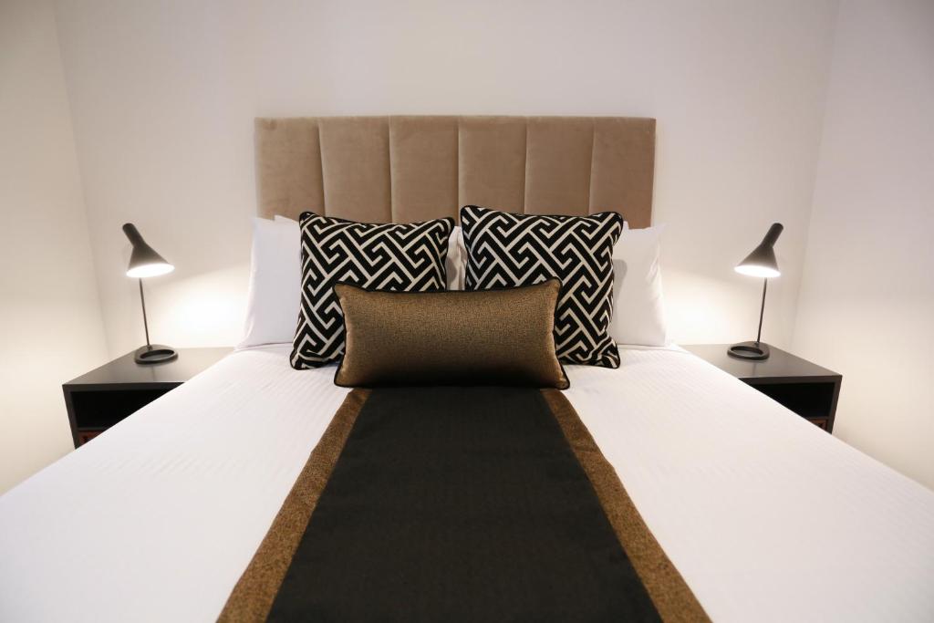 Alex Perry Hotel & Apartments في بريزبين: غرفة نوم بسرير ابيض كبير ومصباحين