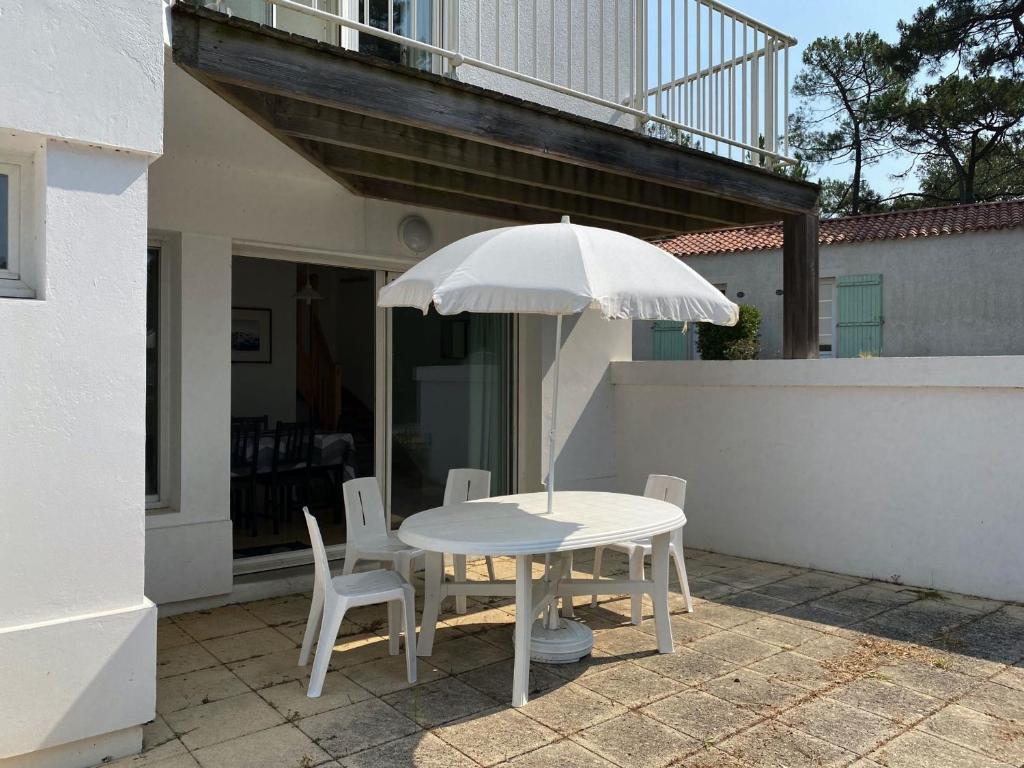 - une table et des chaises blanches avec un parasol sur la terrasse dans l'établissement Longeville-sur-Mer - Pavillon 4 pers, à 850m de la plage, piscine commune - FR-1-336-108, à Longeville-sur-Mer