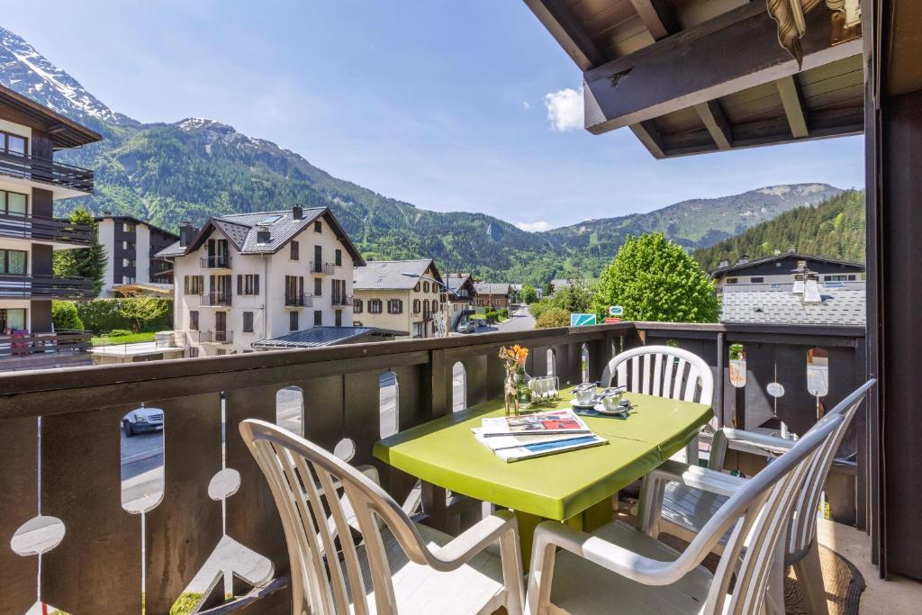 d'une table et de chaises vertes sur un balcon avec vue sur les montagnes. dans l'établissement Appartement Central Des Houches - 15 - Happy Rentals, aux Houches