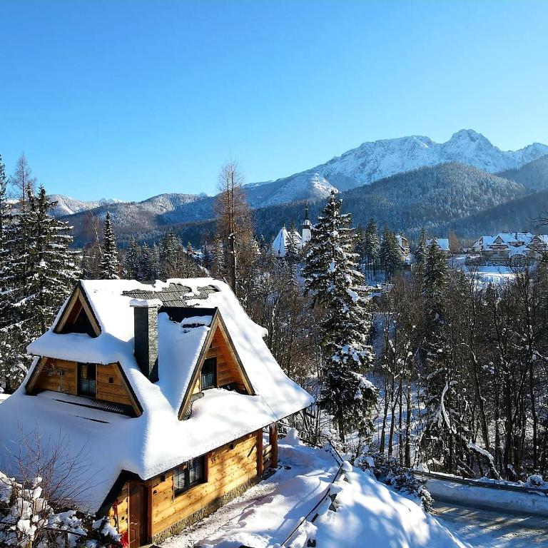 a house covered in snow with mountains in the background at Domek na brzyzku in Kościelisko