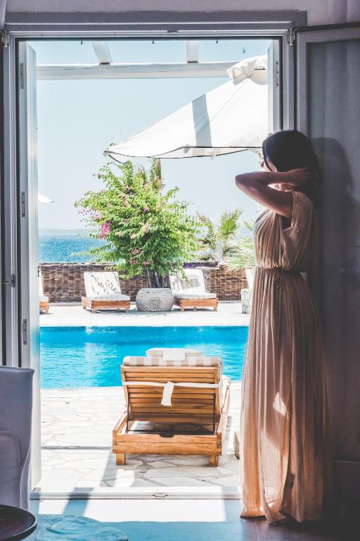 a woman standing in front of a window looking out at the ocean at Hippie Chic Hotel in Agios Ioannis Mykonos