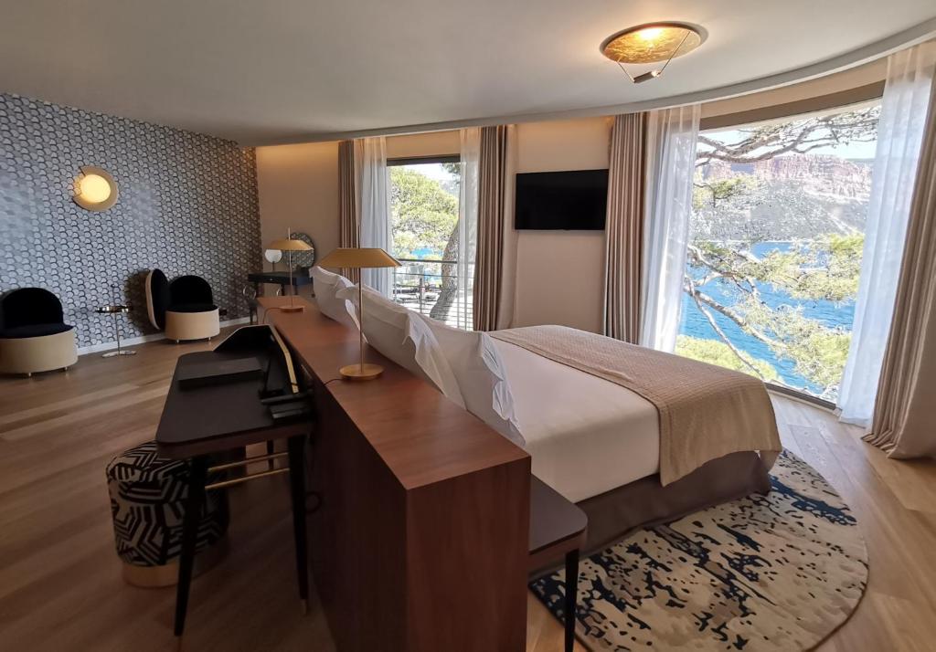 a bedroom with a bed and a desk and a large window at Hôtel Les Roches Blanches Cassis in Cassis