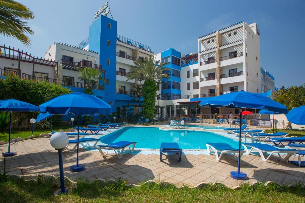 a swimming pool with blue umbrellas and chairs at Hotel Residence Rihab in Agadir